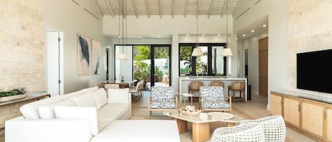 A modern living room with a white sofa, a dining area, and a kitchen with a TV.