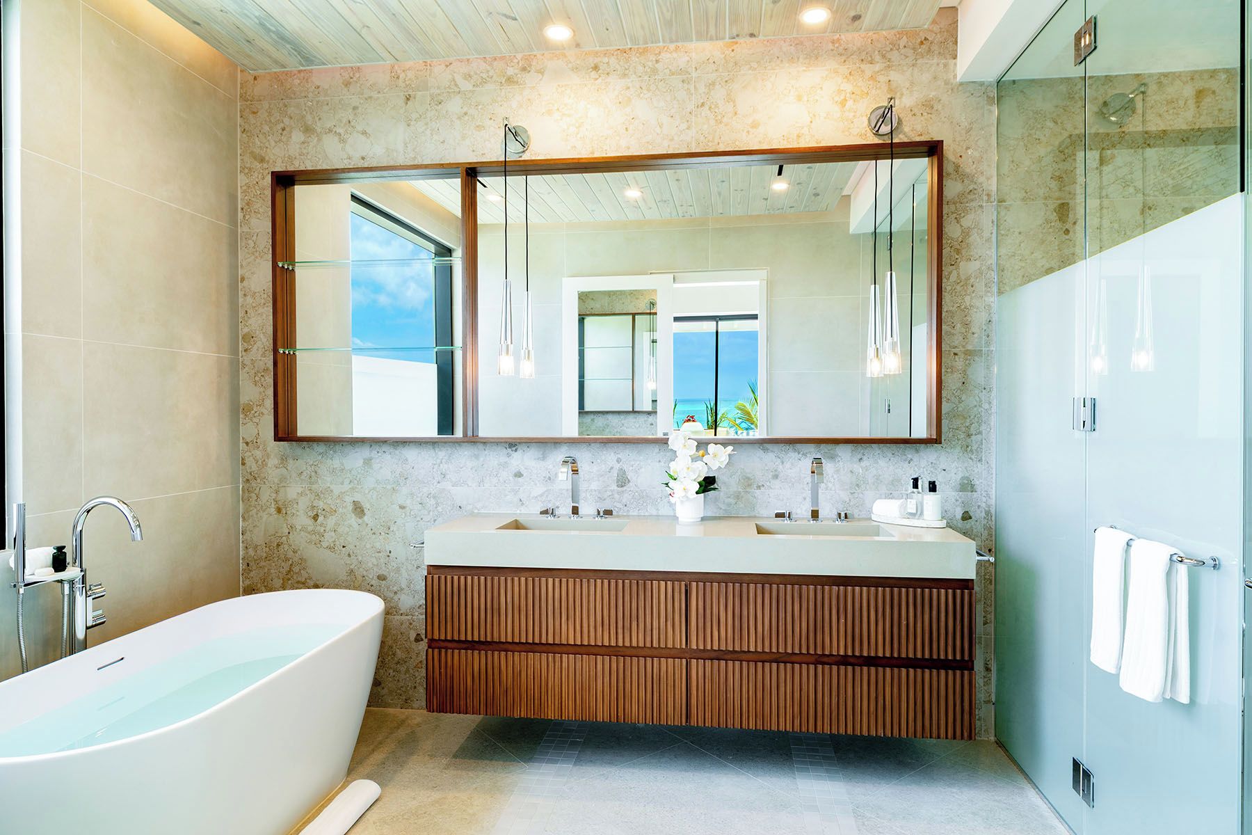 Un bagno moderno con una vasca freestanding, lavabi doppi e un grande specchio che riflette una vista sul mare.