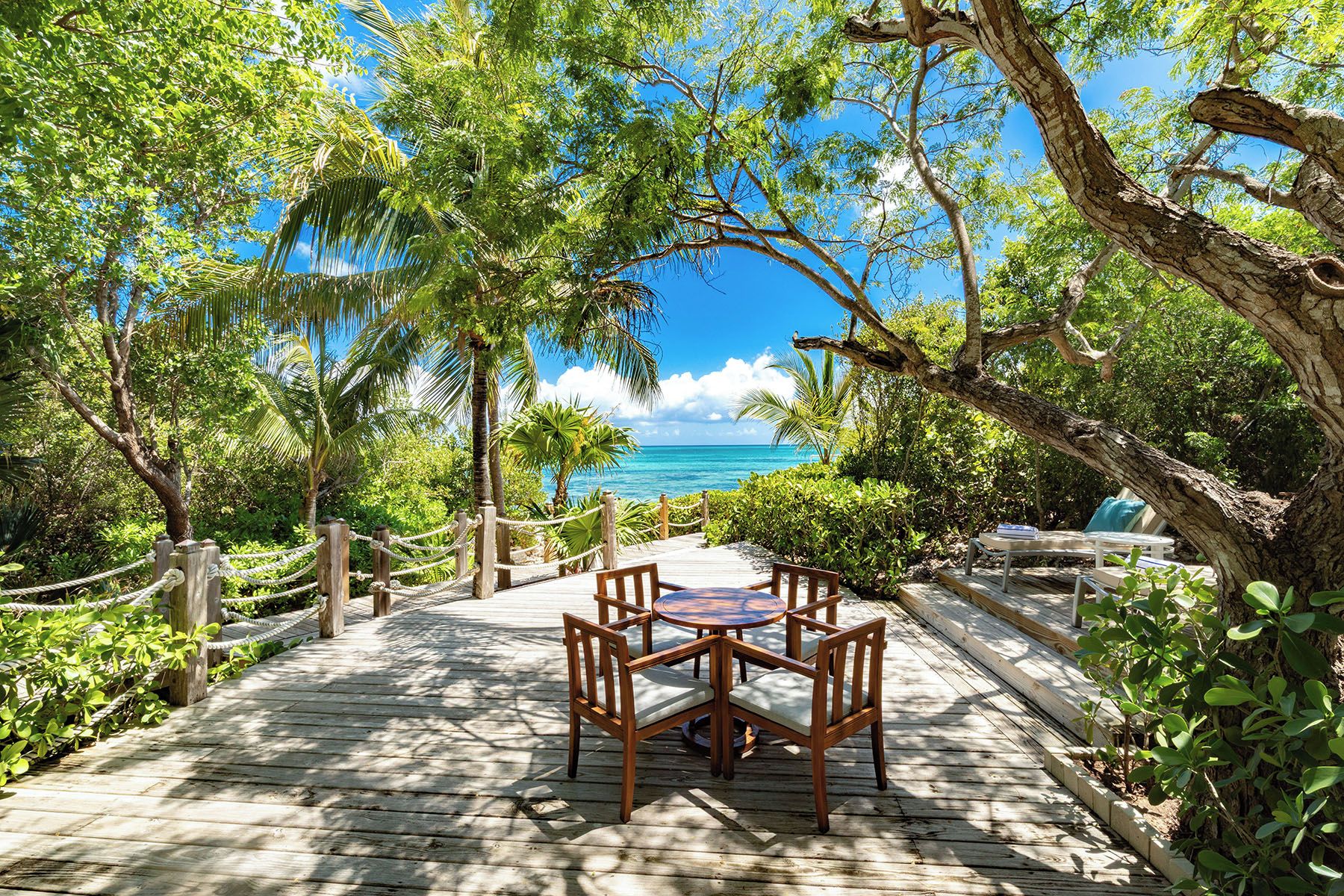 A wooden deck leading to a table and chairs with a view of the ocean.