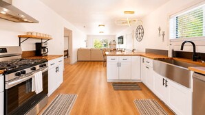 Cocina moderna con estufa, horno y lavabo, suelo de madera y zona de comedor con sofá.