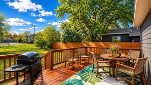 Una terraza de madera con una parrilla, muebles de exterior y un tapete con estampado de hojas tropicales.