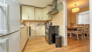 Een moderne keuken met lichte kasten, roestvrijstalen apparatuur en een eethoek met een tafel en stoelen.