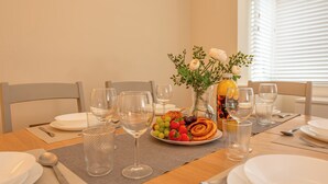 Een eettafel gedekt met borden, bestek, wijnglazen, een fruitschaal en een fles sap.