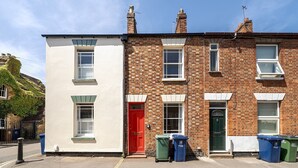 Une rangée de maisons à deux étages, avec une porte rouge, des encadrements de fenêtres blancs et une façade en briques.