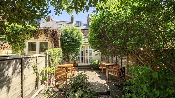 Une terrasse avec des meubles en bois, un petit jardin et une maison avec une fenêtre et une porte.