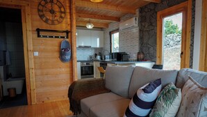 Una sala de estar acogedora con un sofá, cojines, un reloj y una cocina al fondo.