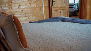 Interior de una cabaña de madera con una cama, una puerta que da a otra habitación y una ventana.