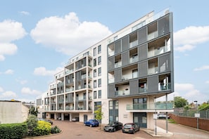 Ein mehrgeschossiges Wohngebäude mit Balkonen, einem Parkplatz und blauem Himmel.