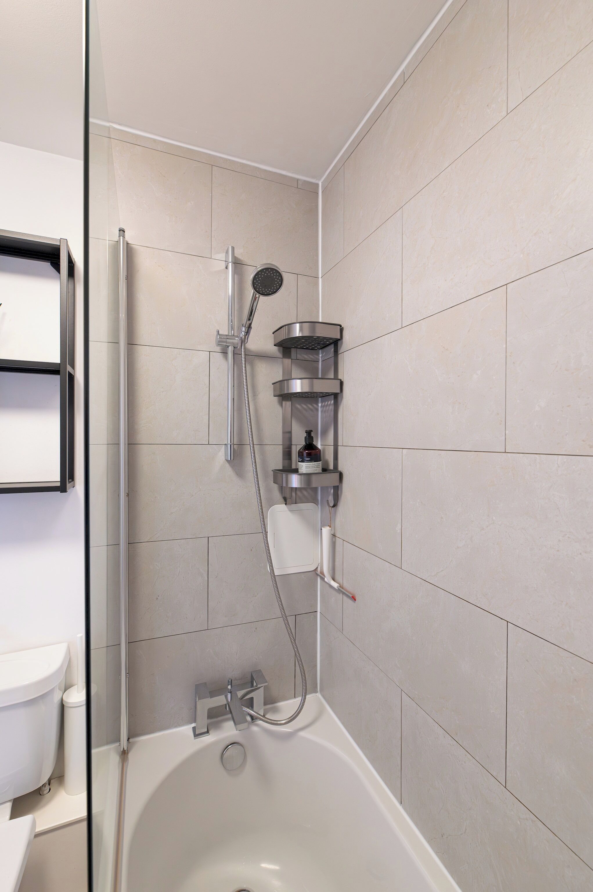 A modern bathroom with a glass-enclosed shower, a white bathtub, and a wall-mounted shelf with toiletries.