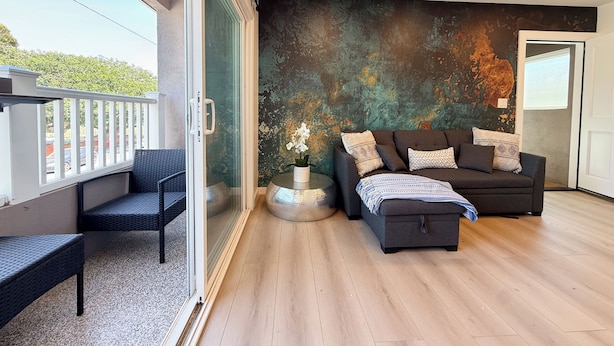 Un salón moderno con un ventanal corredero, un sofá oscuro, una mesita con un jarrón y vistas al exterior.