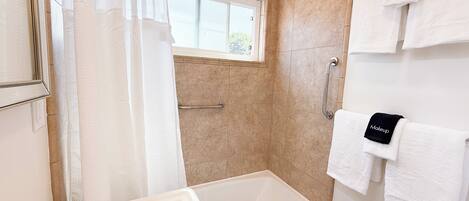 Baño con bañera, ventana, barandilla y toallas con la etiqueta 'Makeup'.