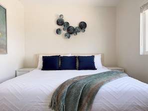 Un dormitorio ordenado con cama, almohadas, una manta y decoración en la pared.