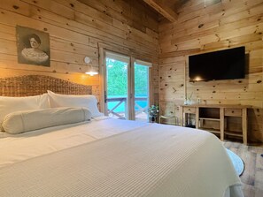 Une chambre dans une cabane en bois, équipée d’un lit, d’une télévision et d’un balcon.