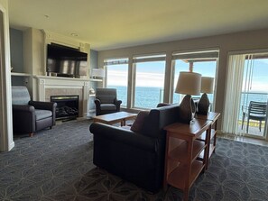 A living room with a fireplace, comfortable seating, a TV, and a view of the ocean. - Charming 2-bedroom condo in Depoe Bay with ocean views (Depoe Bay)