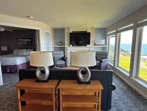 A hotel room with a bed, two armchairs, a TV, and a view of the ocean. - Charming 2-bedroom condo in Depoe Bay with ocean views (Depoe Bay)