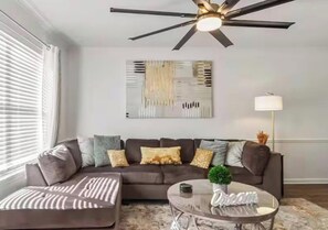 A modern living room with a sectional sofa, a glass coffee table, and a ceiling fan. - Roll Tide Dreams for 6 (Tuscaloosa)