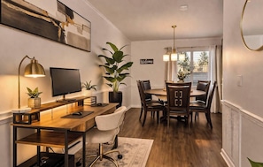 A modern dining area with a wooden table, chairs, a TV, and a large plant. - Roll Tide Dreams for 6 (Tuscaloosa)