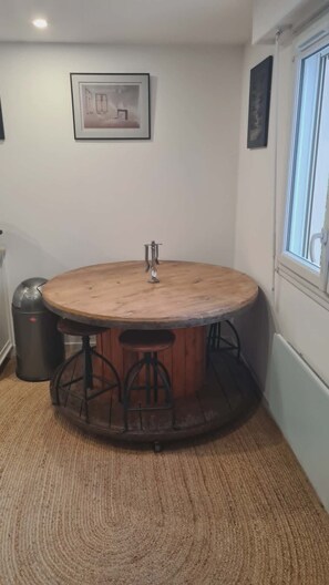 Ein runder Holztisch mit Metallbeinen, eine Mülleimer und ein gerahmtes Bild an der Wand.
