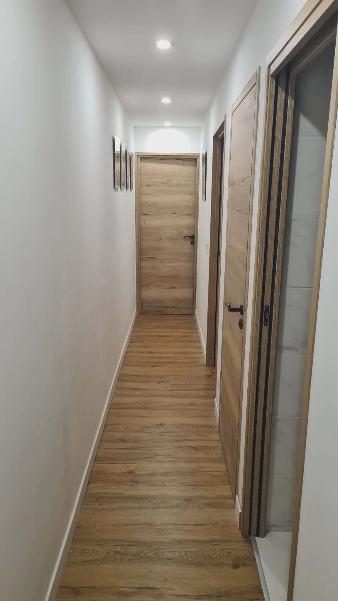 A hallway with wooden flooring, white walls, and doors on both sides.