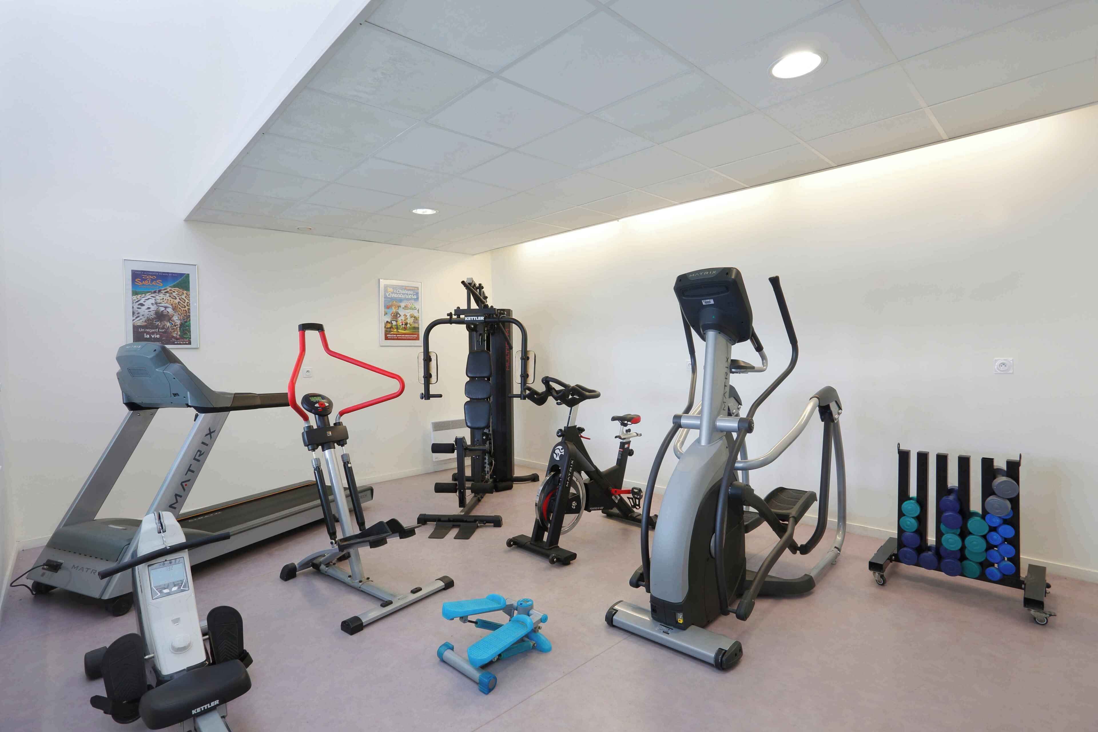 A gym with cardio machines, weightlifting equipment, and a rack of dumbbells.