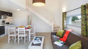 A modern living space with a dining area, a sofa with cushions, a coffee table with magazines, and a staircase.
