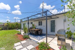 Eine Terrasse mit Tisch und Stühlen, einem Grill und einer Pergola.
