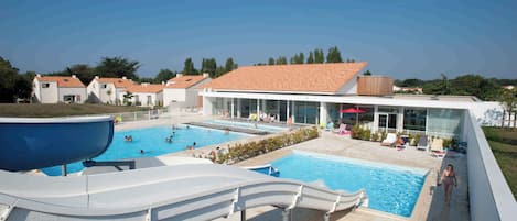 A resort with a swimming pool, lounge chairs, and a water slide.