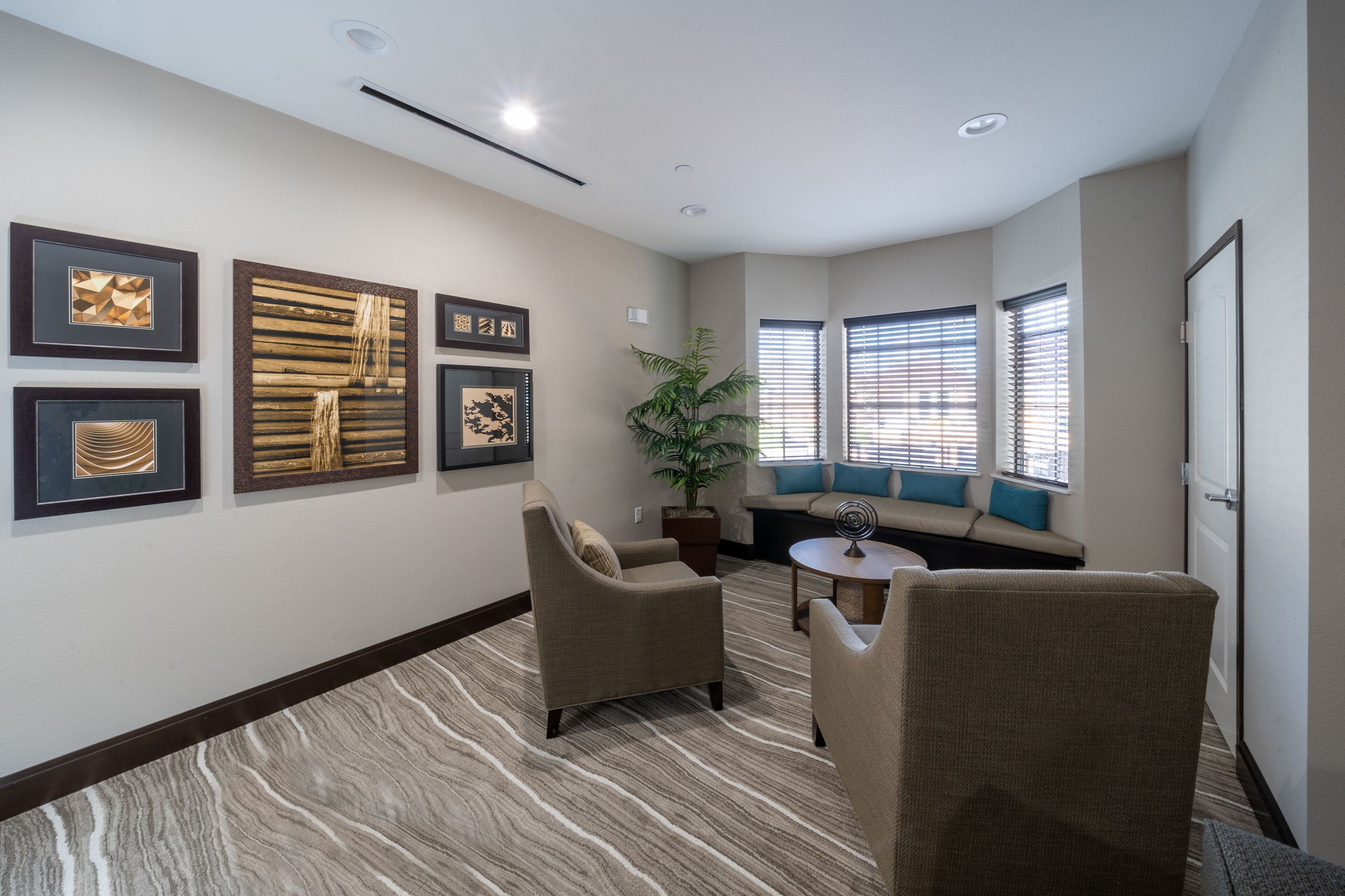A hotel room with a seating area, framed artwork on the walls, and a potted plant.