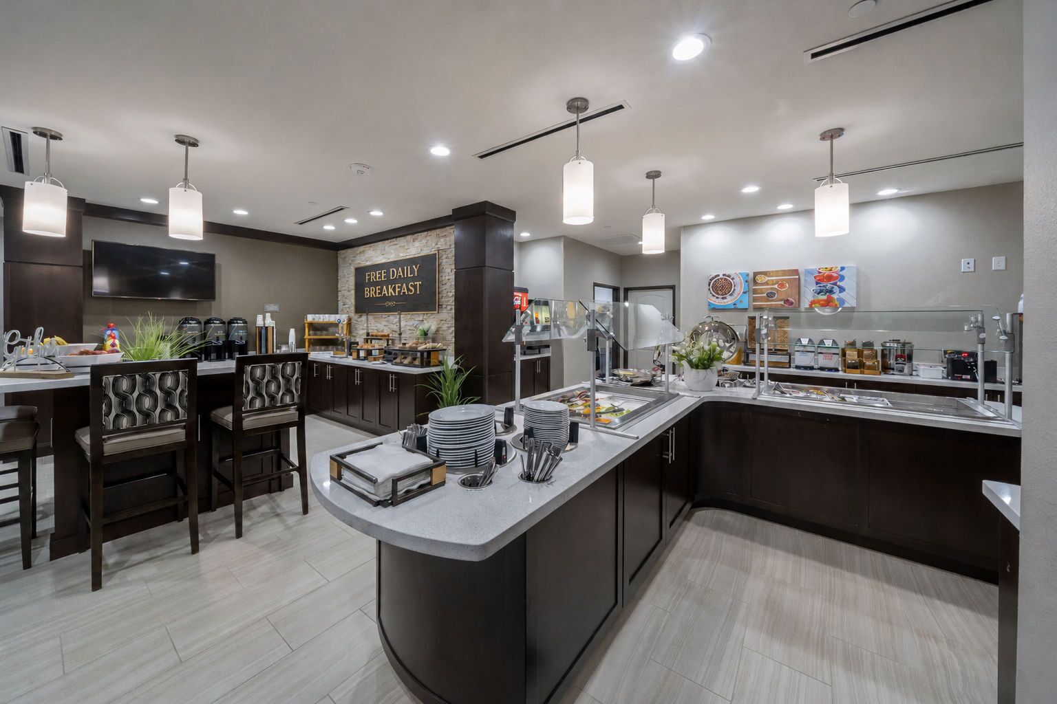 A modern breakfast bar with a sign offering free daily breakfast, a coffee station, and seating with patterned chairs.