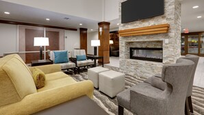 Un hall d’hôtel avec un canapé, des fauteuils, une cheminée et un téléviseur à écran plat fixé à un mur en pierre.