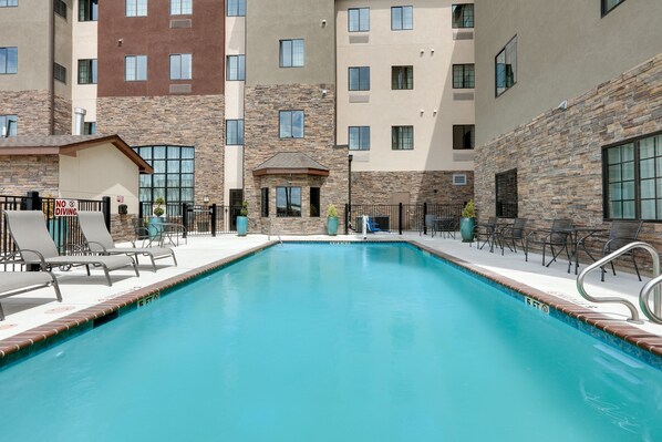 A swimming pool with lounge chairs and a no diving sign, surrounded by multi-story buildings with stone and brick facades. - Spacious 2BR Suite w/ Free Breakfast + Pool (Schertz)