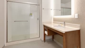 A bathroom with a glass shower door, a sink with a mirror, and a wooden vanity.