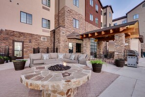 A stone fire pit with a fire, a beige sectional sofa, and outdoor seating. - Spacious 2BR Suite w/ Free Breakfast + Pool (Schertz)