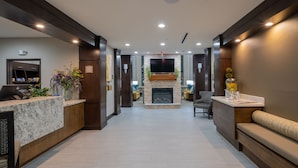A hotel lobby with a reception desk, seating area, fireplace, and a TV mounted on the wall.