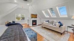 Een slaapkamer in loftstijl met een schuine kap, dakramen, een open haard, een bank en een bed.