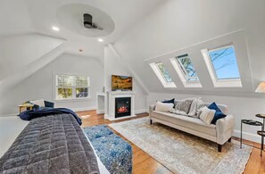 Ein Schlafzimmer im Loft-Stil mit schrägem Dach, Dachfenstern, Kamin, einer Couch und einem Bett.