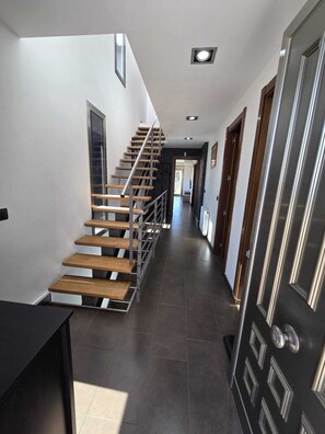 Un intérieur moderne avec un escalier en bois, un revêtement de sol en carrelage foncé et une porte élégante.