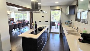 A modern kitchen with a central island, a dining area with chairs, and a view through the glass door. - BEAUTIFUL VILLA  FOR 10 PERSONS, 3 KM FROM THE BEACH OF LLORET IN QUIET LOCATION (Lloret de Mar)