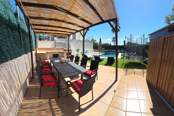 An outdoor patio with a table and chairs, a pool, and a covered area.