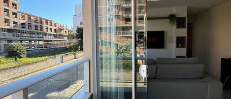 A modern apartment with a balcony, a sofa, and a glass door leading to a city view.