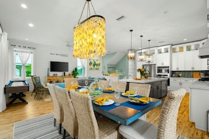 A modern kitchen with white cabinets, a dining area with wicker chairs, and a large chandelier. - Grand Island Retreat: Private Heated Pool | Games (Anna Maria)