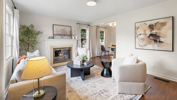 Un salon avec une cheminée, une table basse ronde, un canapé, un fauteuil et un tableau accroché au mur.