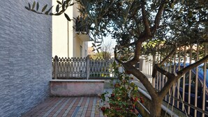 Ein Innenhof mit Backsteinpflaster, einem Baum, einem weißen Zaun und einem Gebäude mit Balkon.