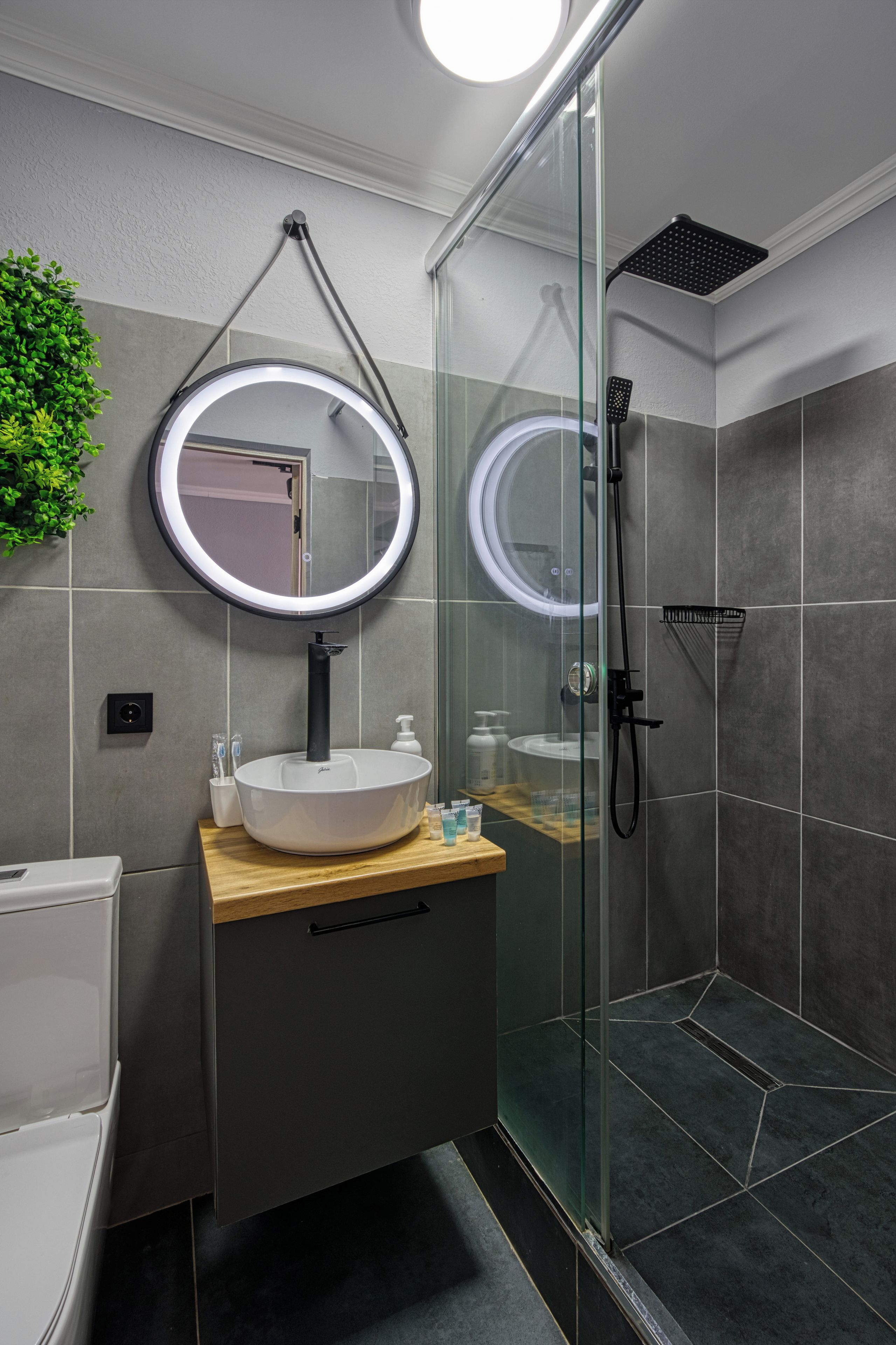 Un baño moderno con un espejo redondo, un lavabo blanco y una zona de ducha con mampara de cristal.