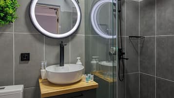 Un baño moderno con un espejo redondo, un lavabo blanco y una zona de ducha con mampara de cristal.