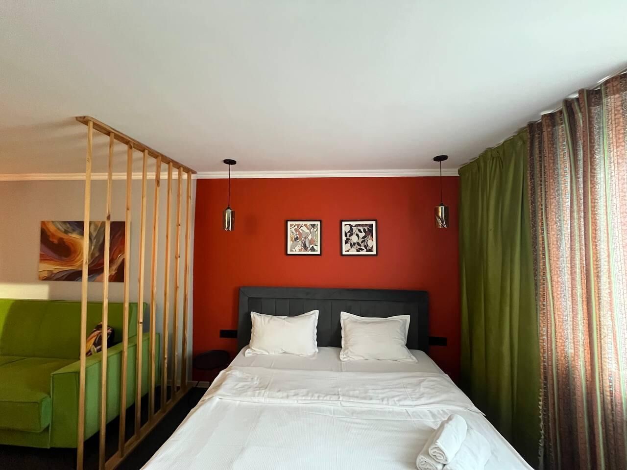 A hotel room with a bed, green armchair, and two framed artworks on the wall.