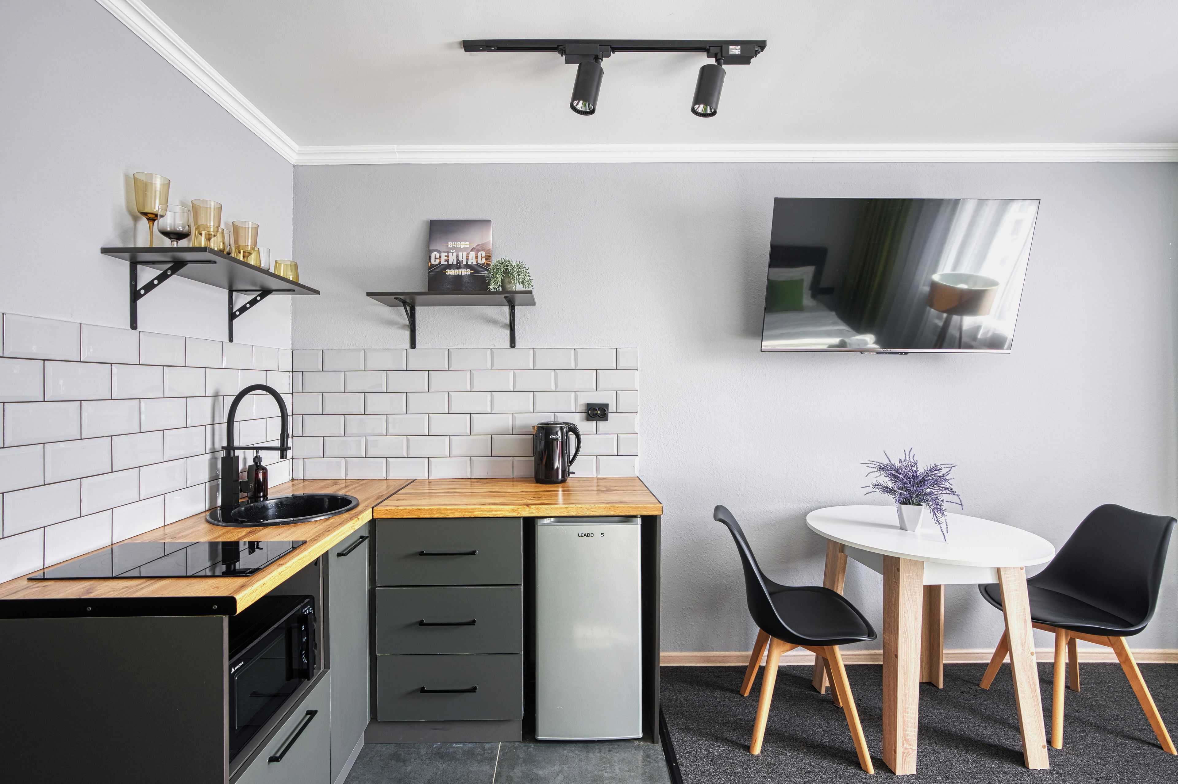 A compact kitchen with a microwave, kettle, and a small refrigerator. There is a dining area with a table and chairs, and a TV mounted on the wall.