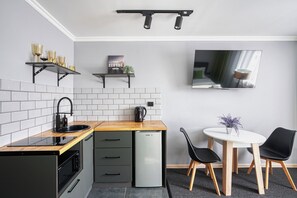 A compact kitchen with a microwave, kettle, and a small refrigerator. There is a dining area with a table and chairs, and a TV mounted on the wall. - The Apartamens 95 (Almaty)