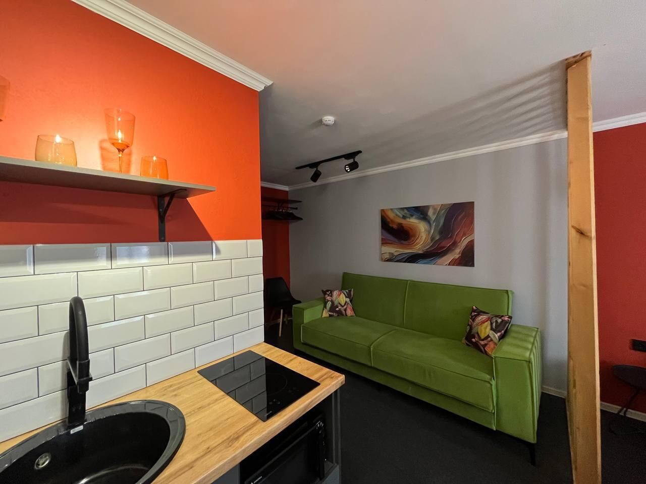 Een compacte kamer met een kitchenette, een groene bank en een schilderij aan de muur.