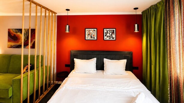 A hotel room with a bed, a green sofa, two wall-mounted lights, and a red accent wall. - The Apartamens 95 (Almaty)